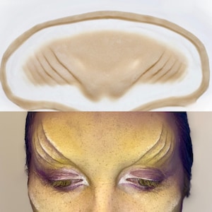 May include: A close-up of a silicone forehead prosthetic with raised lines, designed to create a realistic alien or fantasy creature look. The prosthetic is shown applied to a person's forehead, creating a dramatic effect.