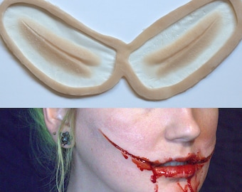 May include: A pair of prosthetic makeup pieces for creating a Joker-style smile. The pieces are made of a flexible, skin-toned material and are designed to be applied to the corners of the mouth.