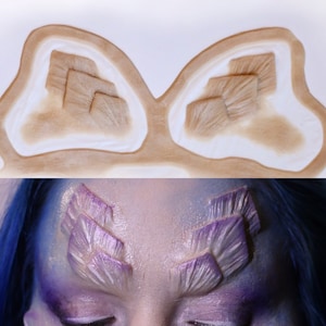 May include: A close-up of a mold for creating special effects makeup. The mold is made of silicone and has two impressions of a geometric pattern. The pattern is made up of overlapping squares.