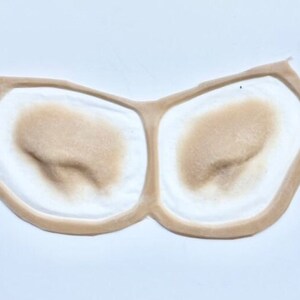 May include: Two beige-colored silicone prosthetic nose shapes, each with a raised, textured surface, are displayed on a white background. The shapes are designed to be used for special effects makeup or cosplay.