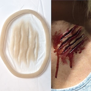 Pode incluir: Um close-up de uma ferida falsa realista, uma prótese de silicone com uma superfície texturizada, projetada para parecer uma profunda marca de garra. A ferida é pintada com tinta vermelha e marrom para simular sangue e carne.