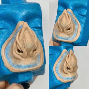 May include: A close-up of a blue sculpture with a tan-colored, organic-shaped element. The tan element is surrounded by a light blue border. The sculpture has a textured appearance and is displayed in multiple views.