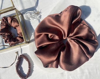 May include: A brown satin scrunchie for hair. The scrunchie is made of soft, silky fabric and is designed to be gentle on hair.