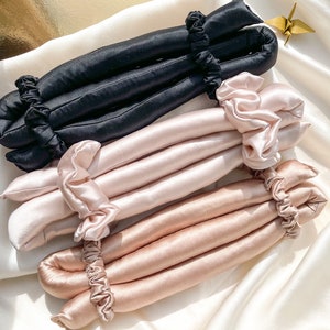 Könnte beinhalten: Drei Sätze Haarrollen, eine schwarze, eine rosa und eine beige, aus weichem Stoff mit Satin-Finish. Die Rollen sind so konzipiert, dass sie Locken und Wellen im Haar erzeugen.