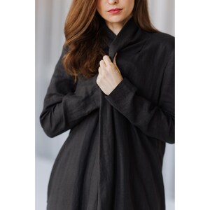 K&ouml;nnte beinhalten: Ein langes, schwarzes Leinenkleid mit drapiertem Ausschnitt und langen &Auml;rmeln. Das Kleid ist aus einem weichen, flie&szlig;enden Stoff gefertigt und wird am Ausschnitt gehalten. Der Gesamtstil ist minimalistisch und elegant.