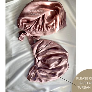 Op de afbeelding: Twee roze satijnen slaapmutsen met een strik aan de zijkant. De tekst "KOBAYASHI DESIGN" is zichtbaar op de bovenste muts. De tekst "PLEASE CHECK ALSO OUR TURBAN CAP" is zichtbaar in de rechterbenedenhoek van de afbeelding.