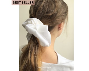 May include: A white scrunchie made of soft fabric, tied in a ponytail on a person's head.