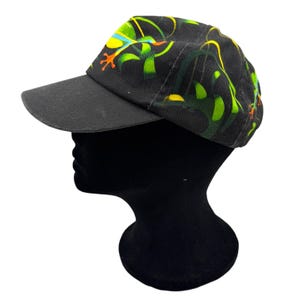 May include: A black baseball cap featuring a vibrant graphic print of a tree frog with bright green, yellow, and orange accents. The cap has a solid black brim and a structured crown, showcasing a detailed illustration of the frog among foliage.