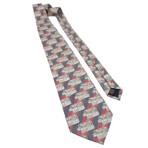 May include: A patterned necktie featuring a repeating design of white buildings on a red and blue background. The tie is made of a smooth fabric and is angled across a white background. The tie is a classic accessory for formal or business attire.