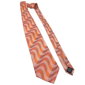 May include: A necktie with a retro wavy pattern in shades of orange, peach, and tan. The tie is angled across a white background, showcasing its design. The tie's fabric appears to have a slight sheen.