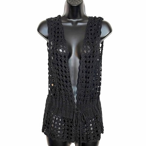 May include: A sleeveless black crochet vest featuring an open-front design with a delicate drawstring tie closure at the waist. The garment is crafted with a repeating diamond-shaped openwork pattern and a solid ribbed knit band around the midsection.