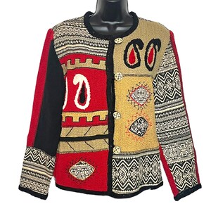 Puede incluir: Un cárdigan rojo, negro y beige con un diseño de patchwork y patrones geométricos. El cárdigan tiene cierre de botón y mangas largas.
