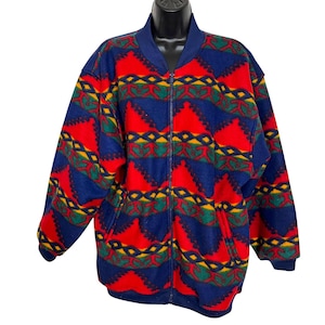 May include: A long-sleeve fleece jacket featuring a vibrant geometric pattern in red, navy blue, green, and yellow. The jacket has a full-length front zipper, a solid navy blue ribbed collar, ribbed cuffs, and two vertical front pockets.