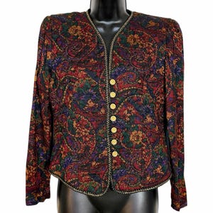 May include: A long-sleeved jacket featuring a multi-colored paisley and floral pattern in shades of red, green, purple, and gold. The garment has a V-neckline, a front button closure with seven gold-toned buttons, and a decorative braided trim along the edges.
