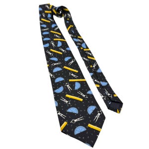 May include: Black necktie with a repeating pattern of yellow rulers, blue protractors, white compasses, and numbers. The tie is made of a smooth fabric and is suitable for formal or professional attire.