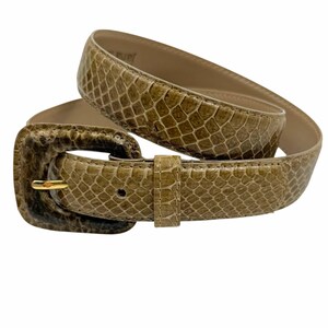 Peut inclure: Une ceinture beige avec une texture façon peau de serpent et une boucle rectangulaire assortie. La ceinture présente un ardillon en métal doré et une doublure intérieure lisse beige clair. La surface extérieure affiche un motif d'écailles.