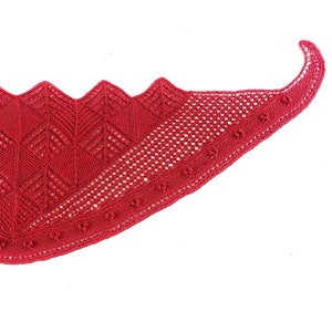 Puede incluir: Un chal de ganchillo rojo con un patrón de encaje. El chal es de forma triangular y tiene un borde festoneado.