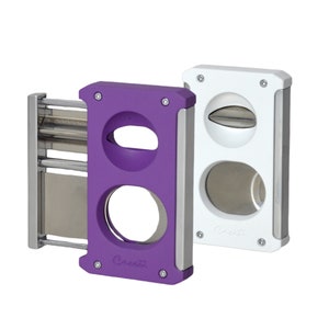 May include: Two cigar cutters, one purple and one white, with silver accents. Both cutters have two different sized circular blades for cutting cigars.