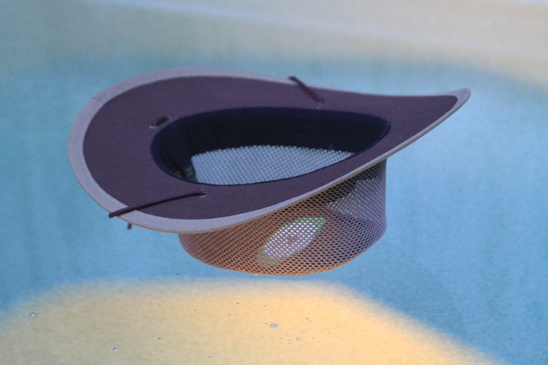 May include: A floating pool skimmer hat with a wide brim. The hat features a dark brown top and a mesh net bottom. The hat is designed to collect debris from the surface of a pool. The hat is floating in a pool of water.