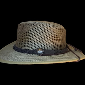 May include: A khaki-colored hat with a mesh crown and a wide brim. The hat features a dark brown braided band with a decorative silver-colored button. A brown drawstring is attached to the hat.