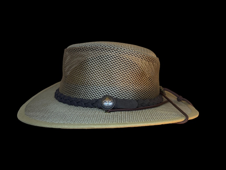 May include: A khaki-colored hat with a mesh crown and a wide brim. The hat features a dark brown braided band with a decorative silver-colored button. A brown drawstring is attached to the hat.