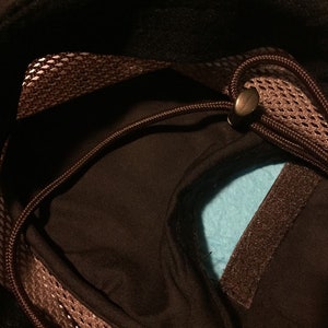 May include: Close-up of a black hat interior with a brown mesh trim and drawstring. A light blue fabric is visible inside the hat. A brown velcro strip is also visible.