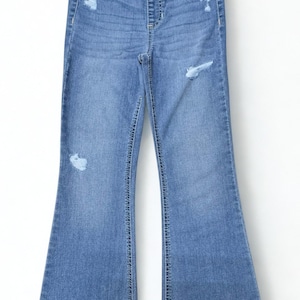 May include: Light blue denim jeans with a flared leg design. The jeans have distressed details on the front and a button and zipper closure. The jeans are a classic style.