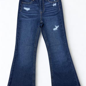 May include: Dark wash denim jeans with a flared leg. The jeans have a high waist, distressed details, and classic five-pocket styling. The jeans are a medium weight and are suitable for everyday wear.