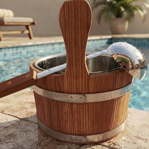 May include: A wooden sauna bucket with a vertical handle and two silver-toned metal bands, featuring a stainless steel interior liner. A matching wooden-handled stainless steel ladle rests inside the bucket, which is covered in small water droplets.