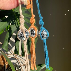 May include: Three handmade macrame keychains with disco ball charms. The keychains are made with natural cotton cord in beige, orange, and teal.