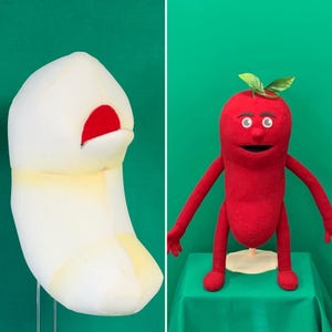 May include: Two quirky puppets. One is a white, abstract form with a red interior. The other is a red, humanoid figure with arms, legs, and a smiling face, topped with green leaves. They are set against a green background.