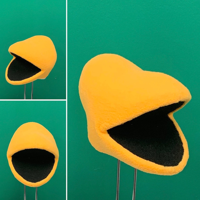 May include: A yellow felt puppet head with a black felt mouth. The puppet head is on a stand.