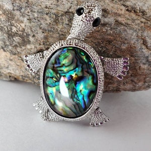 Puede incluir: Un broche de tortuga de plata con una incrustación de concha de abulón verde, azul y morado.
