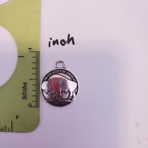 May include: A silver-toned charm featuring a buffalo with the inscription "United States of America Five Cents".