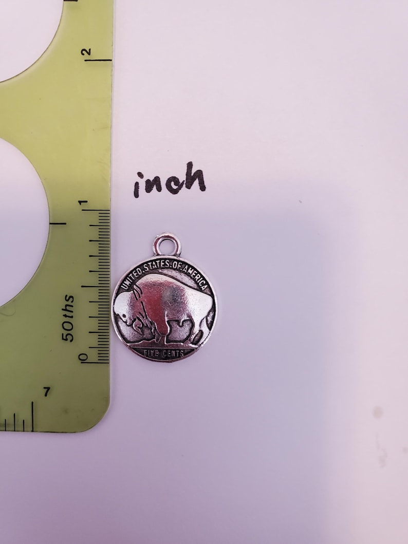 May include: A silver-toned charm featuring a buffalo with the inscription "United States of America Five Cents".