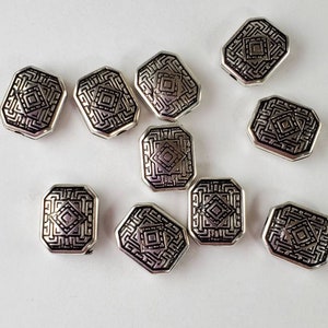 May include: Ten silver-toned metal beads with a geometric design. The beads are octagonal in shape and have a black enamel design.