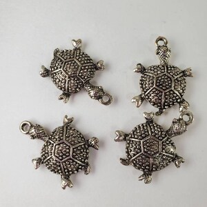 May include: Four silver turtle charms with a textured shell design. The charms have a loop at the top for attaching to jewellery or other crafts.