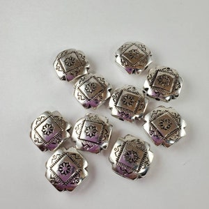 May include: Ten silver-toned metal beads with a square shape and a decorative floral design. The beads have a slightly raised design and a smooth finish.