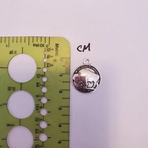 May include: A silver-toned charm featuring a buffalo silhouette with the text "United States of America Five Cents" around the edge. The charm is approximately 2 cm in diameter.