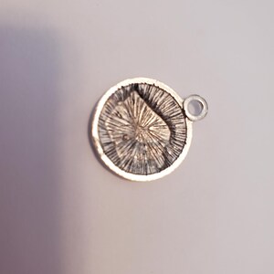 May include: Silver charm with a detailed design of a starburst pattern. The charm has a small loop for attaching to a bracelet or necklace.