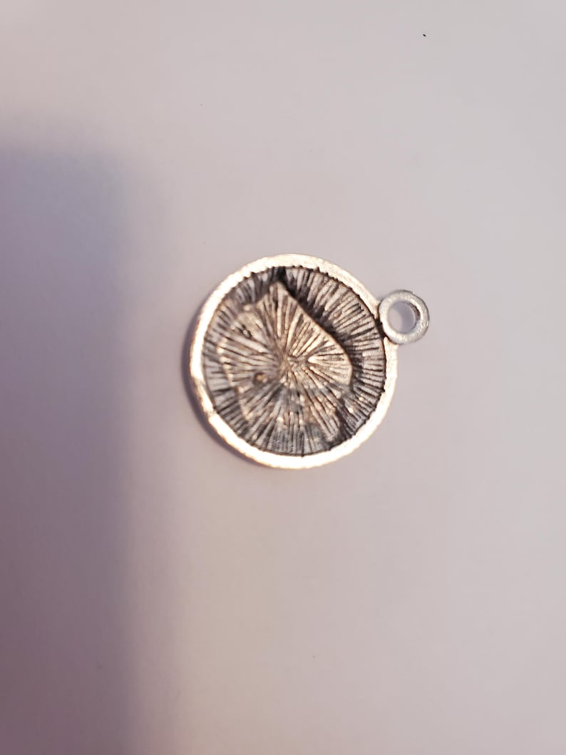 May include: Silver charm with a detailed design of a starburst pattern. The charm has a small loop for attaching to a bracelet or necklace.