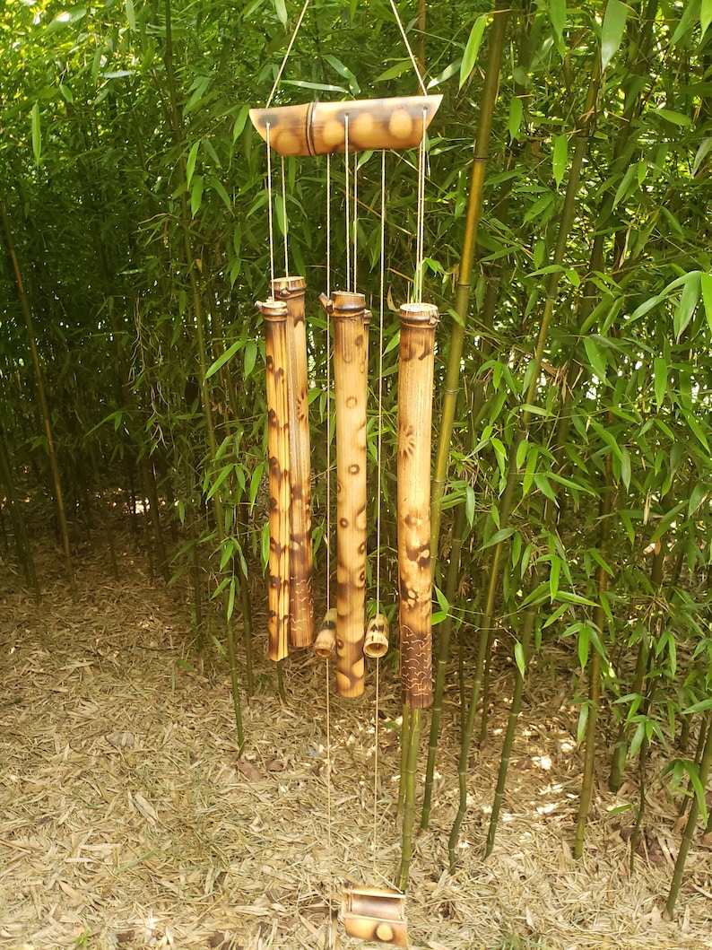 May include: A hanging wind chime constructed from natural bamboo segments. The chime features a horizontal top piece with several vertical hollow bamboo tubes of varying lengths suspended by thin cords, ending in a small bamboo striker at the bottom.