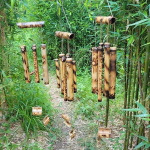 May include: Three hanging wind chimes constructed from cylindrical bamboo segments with natural tan and dark brown scorched markings. Each chime features multiple hollow tubes suspended by strings, creating a vertical arrangement of wood.
