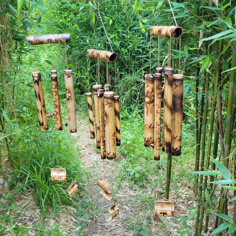 May include: Three hanging wind chimes constructed from cylindrical bamboo segments with natural tan and dark brown scorched markings. Each chime features multiple hollow tubes suspended by strings, creating a vertical arrangement of wood.