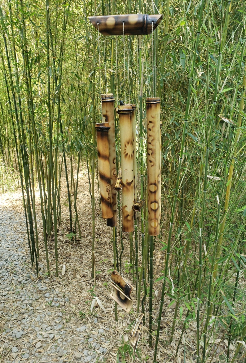 May include: A bamboo wind chime featuring a horizontal top piece and several vertical hollow bamboo tubes of varying lengths. The tubes are decorated with burnt-in circular and geometric patterns, suspended by thin strings from the top support.