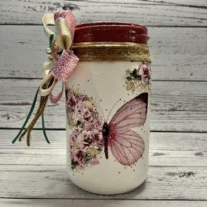 May include: A white mason jar with a pink butterfly and floral design. The jar has a red lid and a brown burlap ribbon around the top.