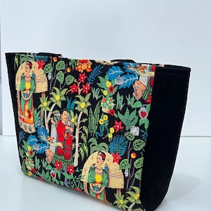 Könnte beinhalten: Schwarze Tragetasche mit einem bunten Blumendruck mit Bildern von Frida Kahlo. Die Tasche hat ein schwarzes Futter und einen schwarzen Griff.