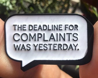 May include: A rectangular speech bubble enamel pin with a white background and a thick black border. The pin features the black text THE DEADLINE FOR COMPLAINTS WAS YESTERDAY in a clean, sans-serif font, centered within the speech bubble shape.