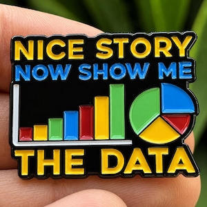 May include: A black enamel pin featuring the yellow text NICE STORY and the blue text NOW SHOW ME, followed by a colorful bar graph and a pie chart, with the yellow text THE DATA at the bottom. The design includes red, yellow, green, and blue.
