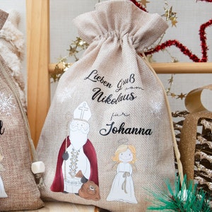 May include: Two beige burlap gift bags with drawstring closures. Each bag features a Santa Claus illustration with the text "Lieben Gruß Nikolaus" and a name. One bag says "Emil" and the other says "Johanna".